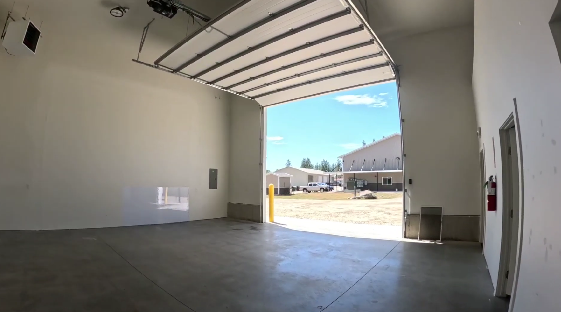 Inside a unit: an open bay door looking out to the gravel yard, concrete slab, and a door through to the private office.