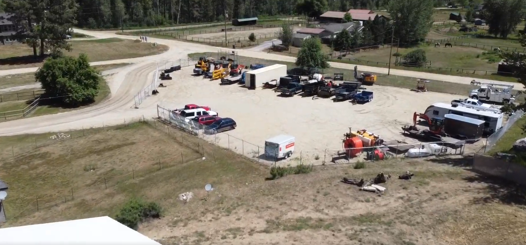 The secure fenced yard, holding skid steers, dump trailers, service trucks, and equipment.