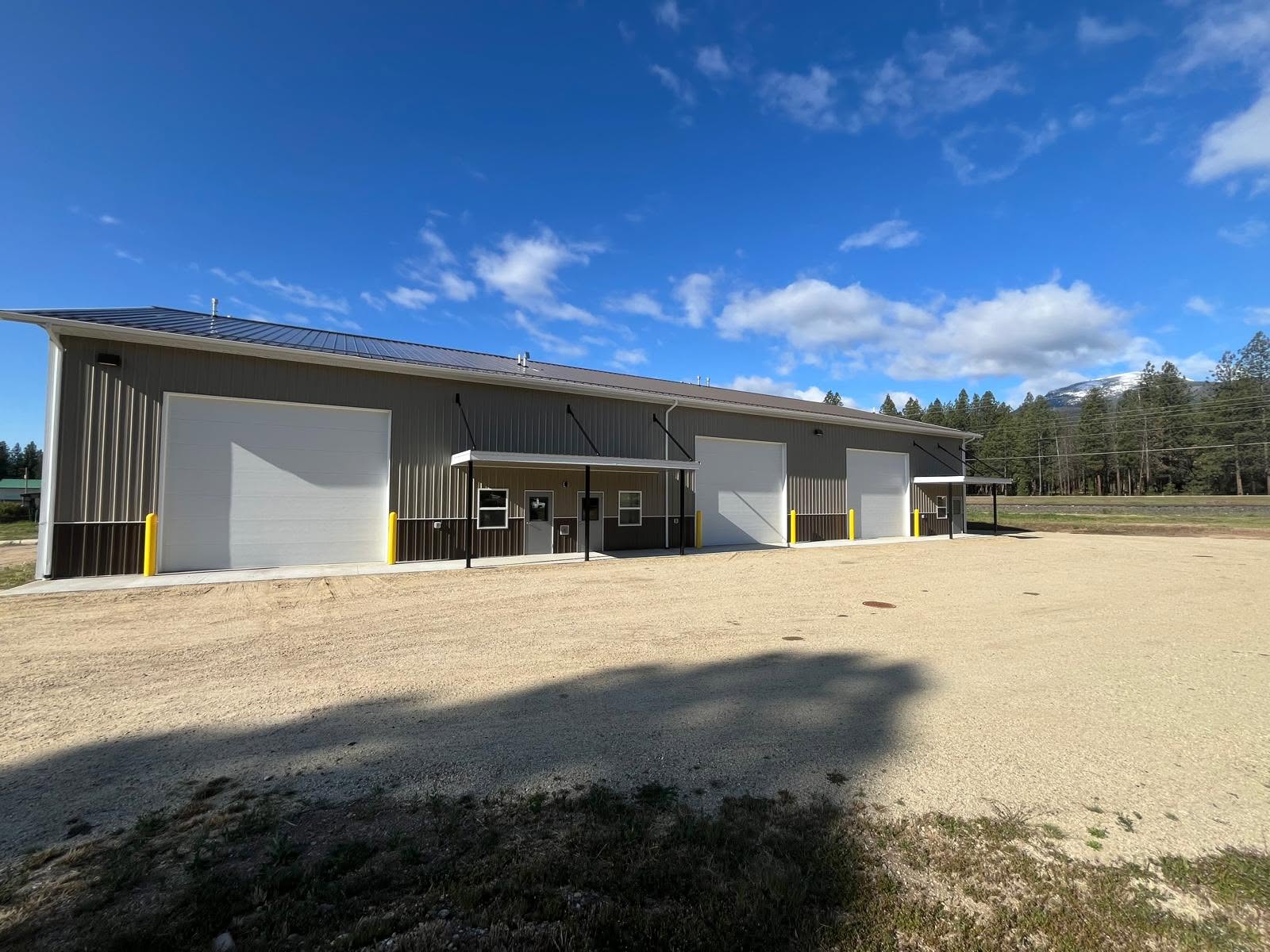 Bitterroot Industrial Park — a metal flex building with white roll-up bay doors, gravel apron, and the Bitterroot Range behind it.